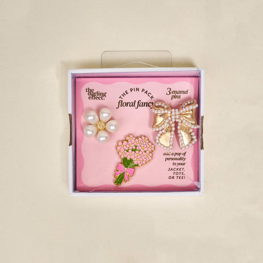 The Darling Effect's Floral Fancy The Pin Pack features three collectible pins—a pearl flower, gold bow with pearl details, and pink bouquet—to add playful charm to your jacket, tote, or tee.