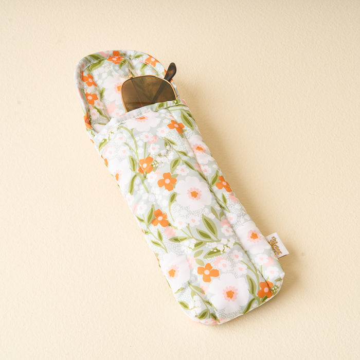 The Darling Effect’s Floral Haven Sage Sunglasses Case features a padded design with a pastel floral pattern of orange and white flowers, green leaves, and holds sunglasses peeking out from the top.