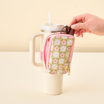 A hand puts a key into The Darling Effect's Flower Check Green Tumbler Fanny Pack, which is attached to the handle of a large cream-colored cup with a straw.
