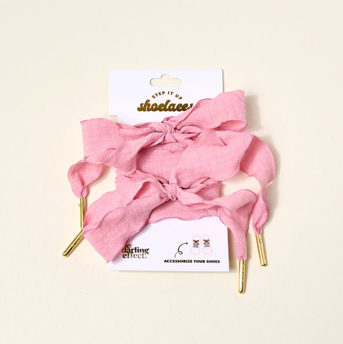 A package of The Darling Effect Frilly Pink Step It Up Shoelaces includes a pair of pink fabric laces with gold tips, displayed on a branded white card featuring icons at the bottom.