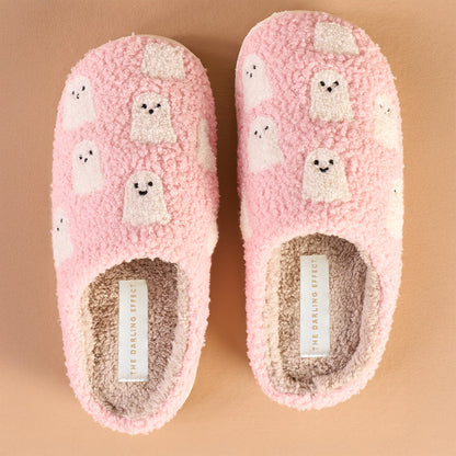 The Darling Effect Ghosts Fuzzy Slippers feature pink fuzz, white cartoon ghost designs, and cream insoles with a visible brand label—perfect fall-themed slippers shown side by side on a beige background.