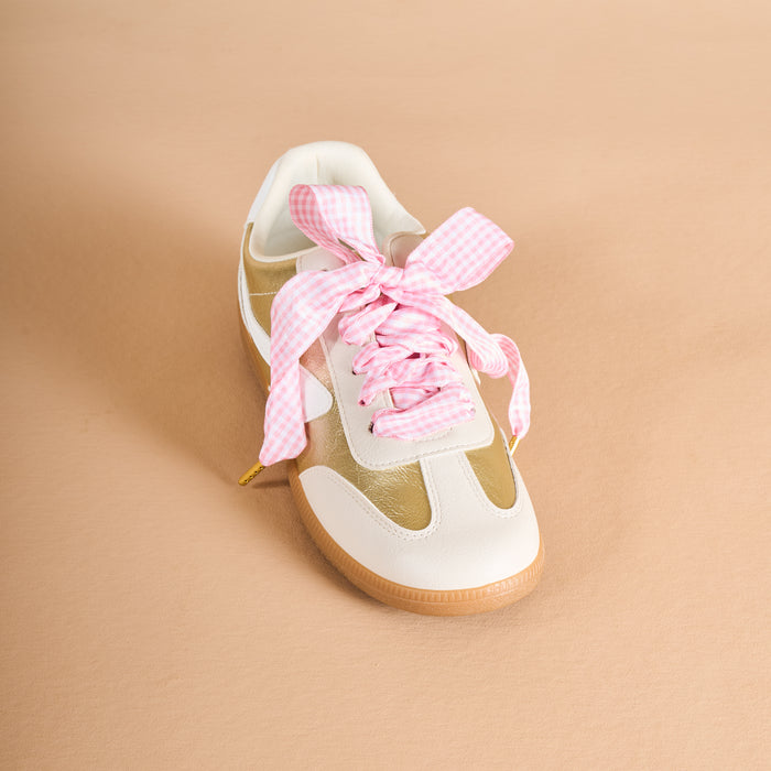 A white and beige sneaker with a gum sole is shown on a tan background, featuring The Darling Effect's Gingham Pink Step It Up Shoelaces laced in a wide, pink-and-white checkered bow.