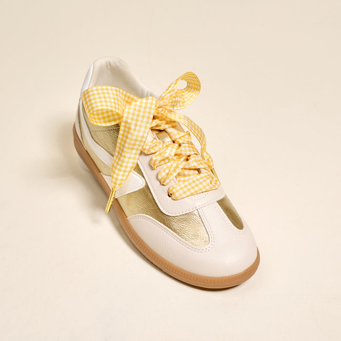 The Darling Effect’s Gingham Yellow Step It Up Shoelaces add a yellow and white gingham bow accent to your white and gold sneakers with a gum sole—perfect for making a statement against any neutral background.