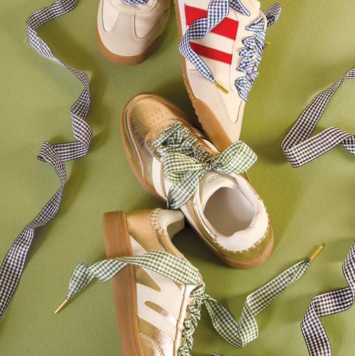 Three pairs of sneakers featuring The Darling Effect’s Gingham Yellow Step It Up Shoelaces are displayed on a green background.