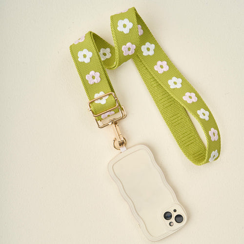 The Darling Effect's Green Hold the Phone Crossbody Strap, featuring a white and pink flower pattern, is attached to a cream phone case.