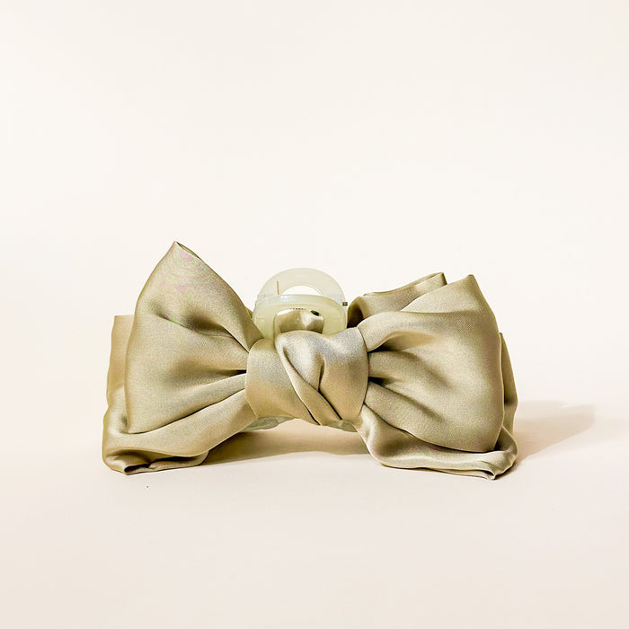 The Darling Effect's Green Satin Bow Claw Clip features a neatly tied satin bow with a translucent round center, creating an elegant hair accessory for updos, displayed on a plain off-white background.