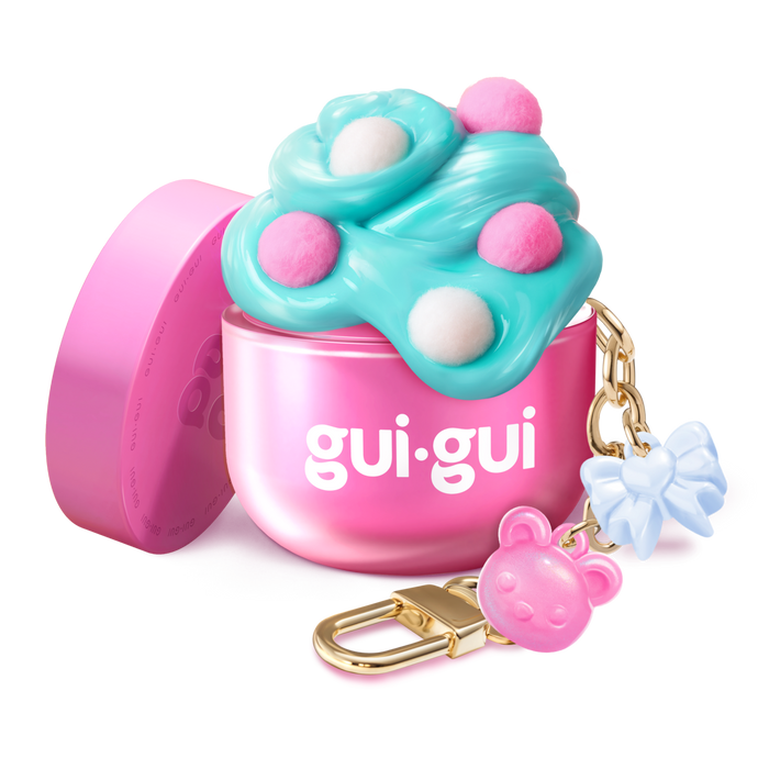 The Gui Gui Mini Backpack Charm Slime by Moose Toys is a small pink container with blue and pink fluffy slime, white and pink dots, plus a gold keychain featuring a pink bear charm and a blue bow charm.