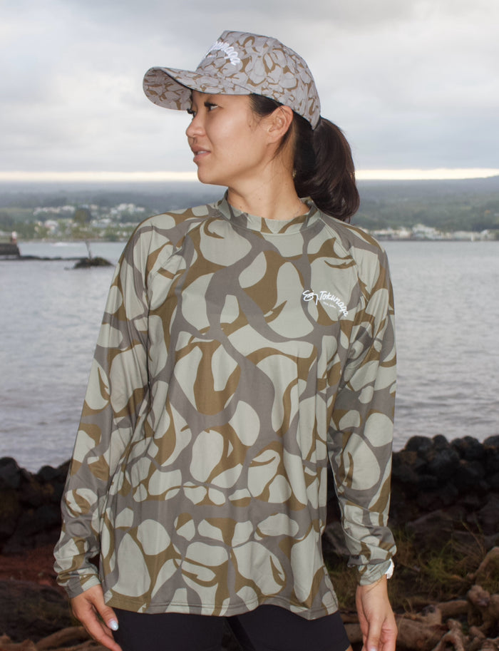 Person wearing a camouflage long-sleeve shirt and cap by a body of water.