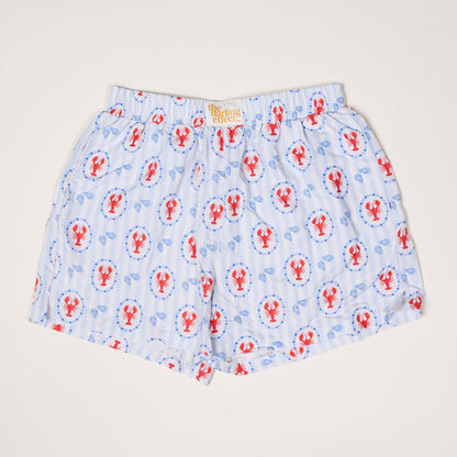 The Darling Effect’s Harbor House All Day Boxer Shorts feature light blue and white stripes with red lobsters and blue lifebuoys, a comfy elastic waistband, breathable fabric, and a signature label—ideal for trendy loungewear.