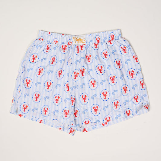 The Darling Effect’s Harbor House All Day Boxer Shorts feature light blue and white stripes with red lobsters and blue lifebuoys, a comfy elastic waistband, breathable fabric, and a signature label—ideal for trendy loungewear.