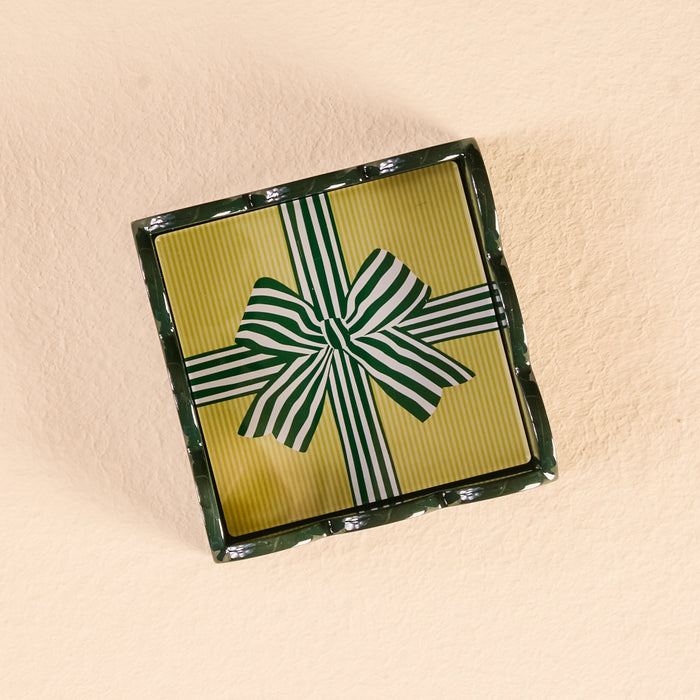 A rectangular gift box with a yellow, green, and white striped lid and bow displays The Darling Effect’s Holiday Gift Bow Green Scallop Trinket Tray, perfect for gifting, set on a light beige textured surface.