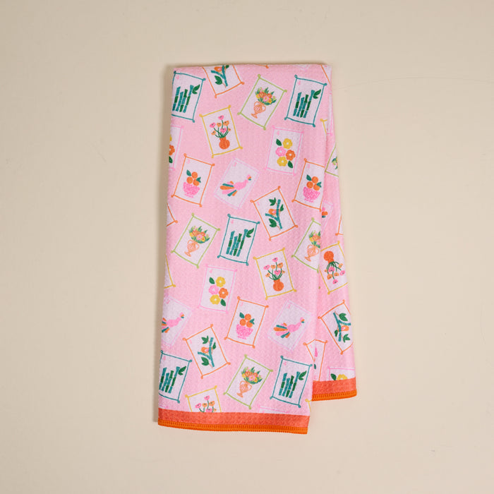 The Darling Effect's "It's Mahj Time" Waffle Tea Towel features a colorful, framed floral pattern with orange edging. This absorbent pink kitchen towel adds a cheerful touch and is shown folded neatly on a light beige background.