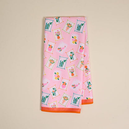 The Darling Effect's "It's Mahj Time" Waffle Tea Towel features a colorful, framed floral pattern with orange edging. This absorbent pink kitchen towel adds a cheerful touch and is shown folded neatly on a light beige background.