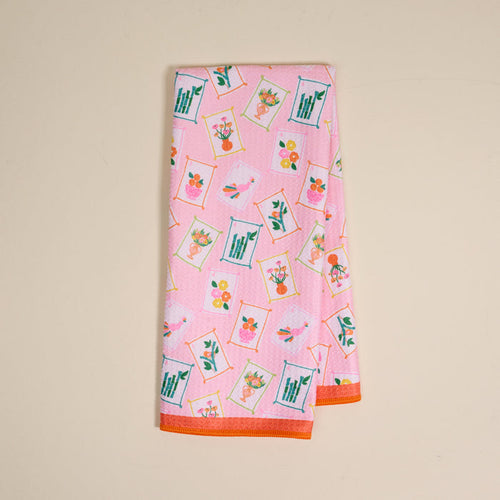 The Darling Effect's "It's Mahj Time" Waffle Tea Towel features a colorful, framed floral pattern with orange edging. This absorbent pink kitchen towel adds a cheerful touch and is shown folded neatly on a light beige background.