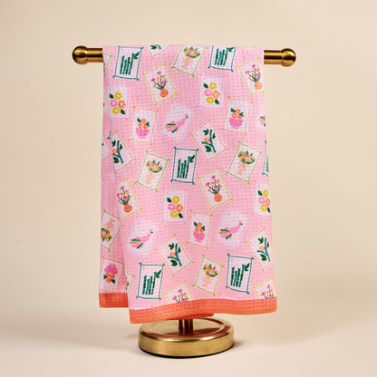The Darling Effect’s “It’s Mahj Time” Waffle Tea Towel, a pink and absorbent kitchen towel, hangs neatly on a gold stand against a beige background.