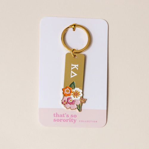 The Darling Effect's Kappa Delta Enamel Keychain features Greek letters and colorful flower designs, attached to a display card labeled "thats so sorority COLLECTION," making it an ideal gift for any Kappa Delta sister.