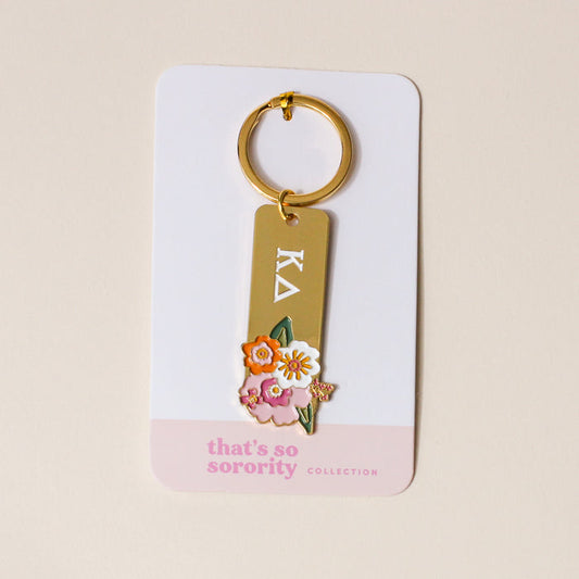 The Darling Effect's Kappa Delta Enamel Keychain features Greek letters and colorful flower designs, attached to a display card labeled "thats so sorority COLLECTION," making it an ideal gift for any Kappa Delta sister.