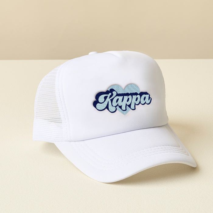 The Darling Effect's Kappa Kappa Gamma White Trucker Hat features "Kappa" in blue script on a blue heart patch—an ideal embroidered sorority hat or sisterhood gift. Displayed on a cream surface with a beige background.