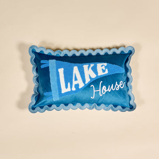 The Darling Effect Lake House Scalloped Rectangle Throw Pillow features a blue design with scalloped edges and “LAKE” and “House” embroidered on a light beige background.