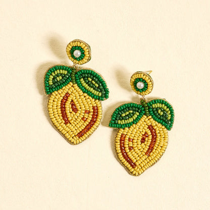 Lemon Beaded Earrings by The Darling Effect are vibrant, hand-beaded earrings featuring yellow, orange, and green beads shaped like lemons with leafy details, displayed on a light beige background.