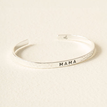 The Darling Effect's Little Reminder Cuff is a silver bracelet engraved with "MAMA" and a small "el" initial inside—a thoughtful, everyday mantra piece.