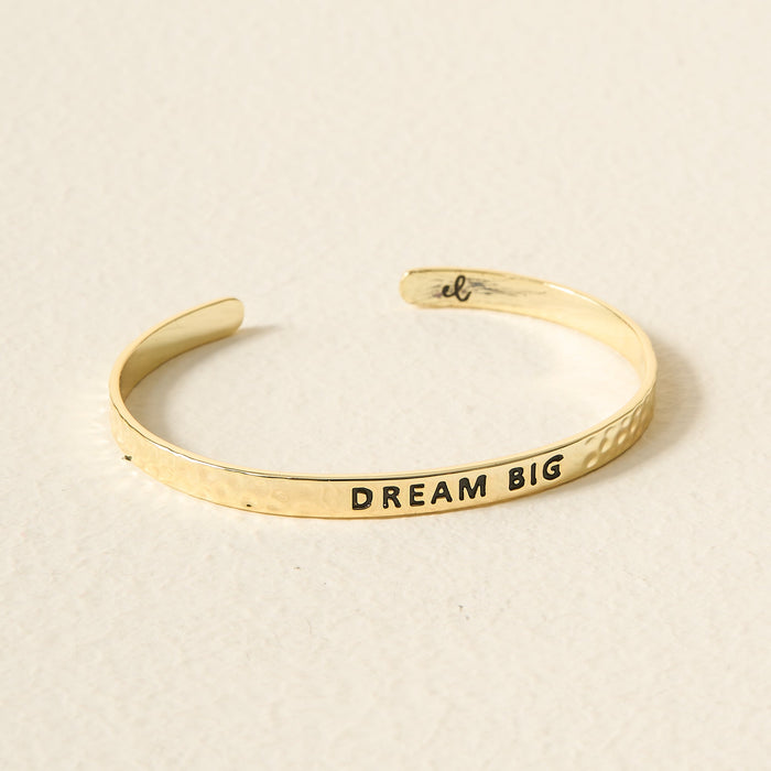 The Darling Effect's Little Reminder Cuff is a 14k gold cuff bracelet with a hammered outer texture and DREAM BIG engraved inside in black, offering adjustable fit and daily inspiration.
