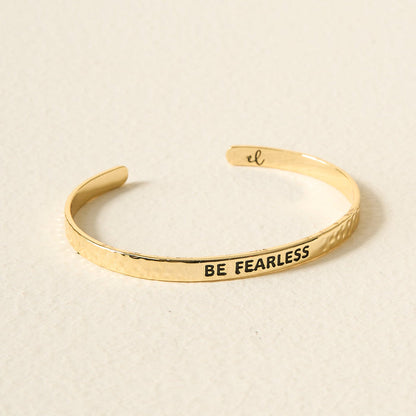 The Darling Effect's Little Reminder Cuff features BE FEARLESS engraved on 14k gold, displayed on a light, textured surface—the perfect mantra bracelet.