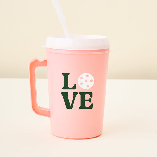 The Darling Effect Love Pickleball 34 oz Mega Mug: pink tumbler with handle, white lid, and straw. Features dark green "LOVE" text with a pickleball graphic as the O.