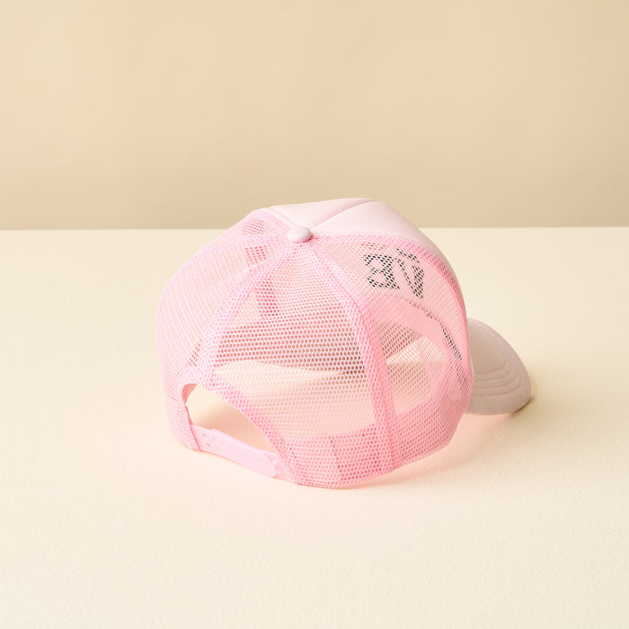 The LOVE Pickleball Trucker Hat by the-darling-effect is shown from the back on a beige surface, displaying its light pink mesh, adjustable strap, and partially visible trendy black phrases on the mesh.