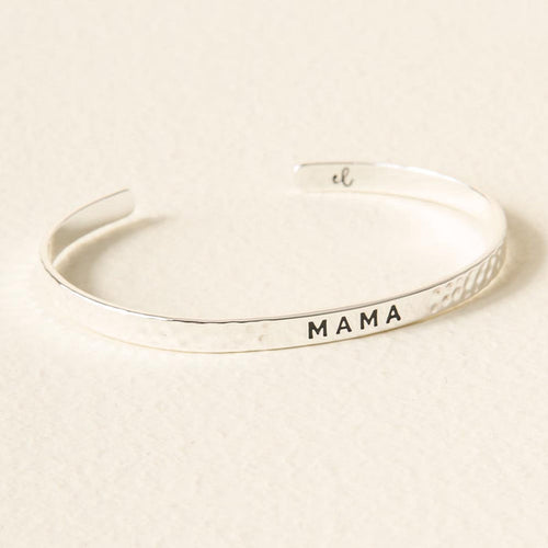 The Darling Effect Mama Cuff Bracelet features a silver hammered texture and "MAMA" engraved in black on the front, displayed elegantly on a light surface.
