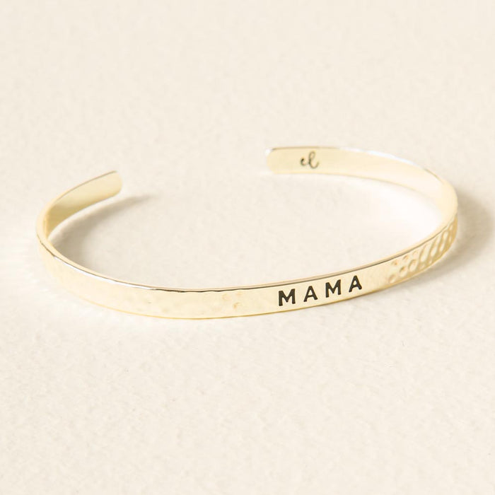 The Darling Effect’s Mama Cuff Bracelet is an adjustable gold piece with "MAMA" engraved on its hammered surface, displayed on a light beige background—the ideal Little Reminder Cuff.