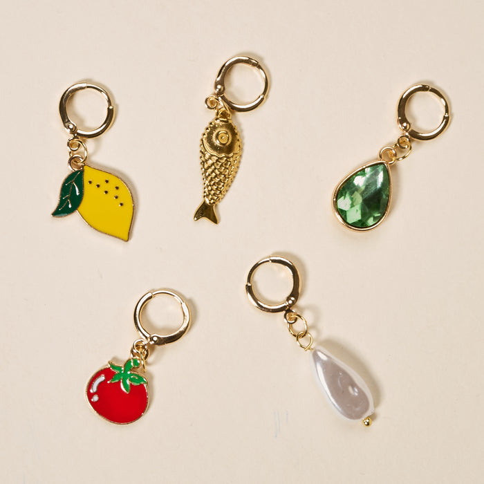 Mediterranean Muse The Ultimate Charm Pack by The Darling Effect includes five gold hoop earrings with playful charms: yellow lemon, textured gold fish, green teardrop gem, red tomato, and white pearl—perfect for vibrant style.