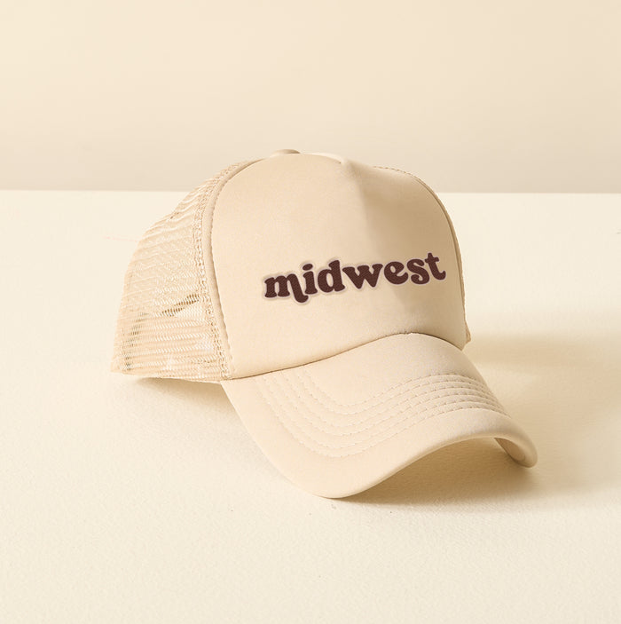 The Darling Effect's Midwest Trucker Hat is a beige mesh cap featuring "midwest" in brown embroidered lettering on the front, shown on a light surface with a neutral background.