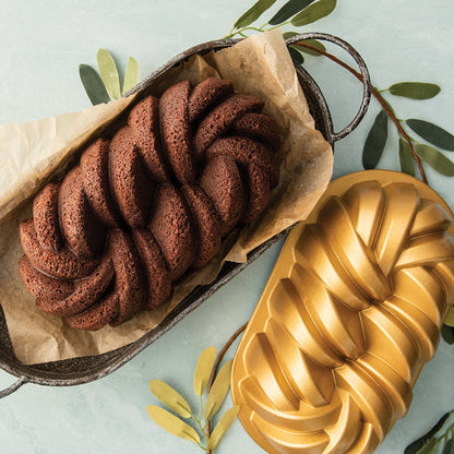 Braided chocolate bread in a loaf pan with a decorative mold on a light green background.