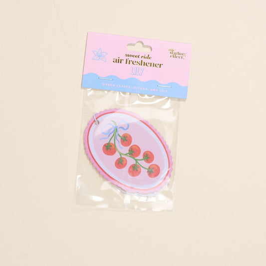 The Darling Effect Off the Vine Sweet Ride Car Air Freshener offers a long-lasting blend of green leaves, citrus, and lily notes for a fresher drive. Features a playful tomato design with a blue bow.
