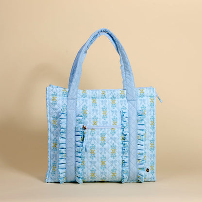 The Darling Effect's Oh So Fancy Blue The Everyday Quilted Tote Bag features a light blue floral design, ruffled trim, and two straps—ideal for daily errands or as a chic travel tote on your next adventure.