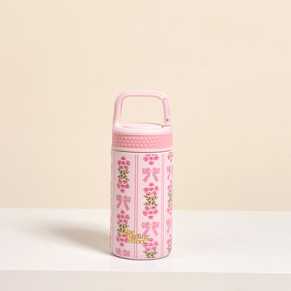 The Darling Effect’s Oh So Fancy Pink 6 oz Lil' Bitty Bottle stands upright on a white surface with floral and bow designs, gold “A little perfect” text, and a textured handle—an ideal travel companion for on-the-go hydration.