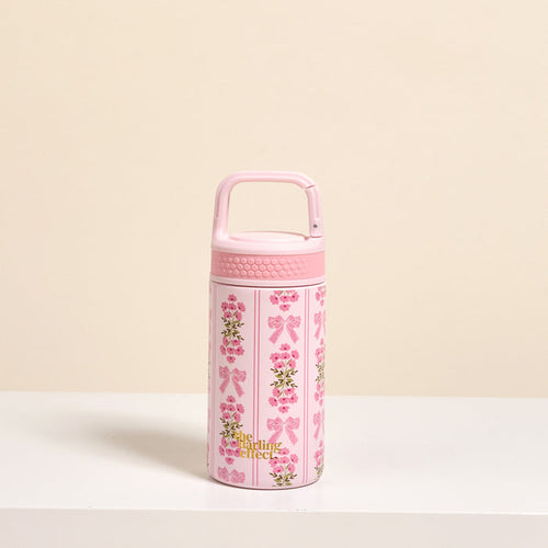 The Darling Effect’s Oh So Fancy Pink 6 oz Lil' Bitty Bottle stands upright on a white surface with floral and bow designs, gold “A little perfect” text, and a textured handle—an ideal travel companion for on-the-go hydration.