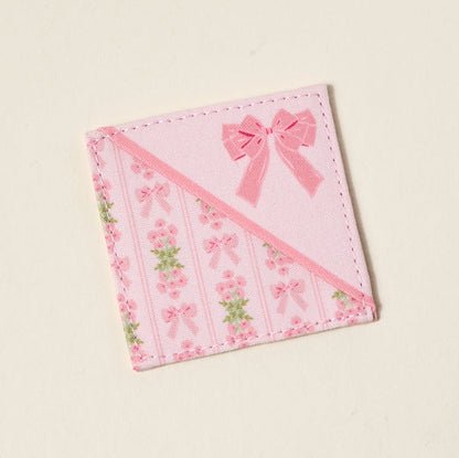 The Darling Effect’s Oh So Fancy Pink Corner Keeper Fabric Bookmark features printed roses, pink bows, and green leaves in diagonal stripes with a large bow accent—a cute book lover gift and perfect for marking your place in style.