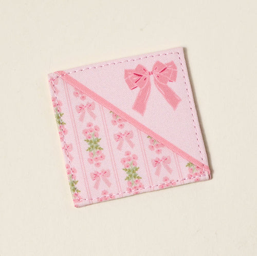 The Darling Effect’s Oh So Fancy Pink Corner Keeper Fabric Bookmark features printed roses, pink bows, and green leaves in diagonal stripes with a large bow accent—a cute book lover gift and perfect for marking your place in style.