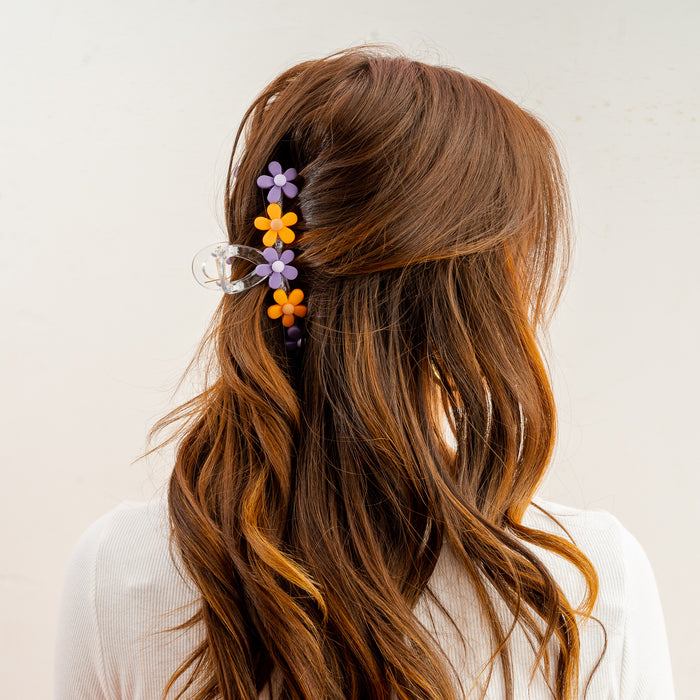 A woman with long, wavy brown hair is seen from behind, wearing The Darling Effect’s Orange Purple Game Day Daisy Claw Clip in her hair, paired with a white top against a plain background—perfect for showing school spirit.