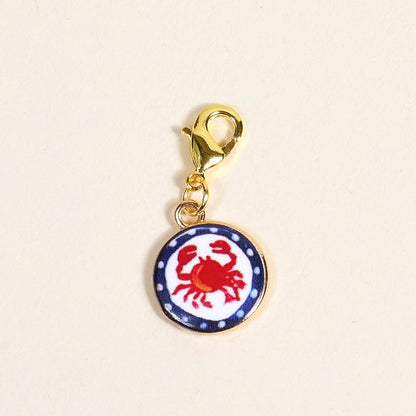 The Darling Effect Painted Crab Jewelry Charm Gold features a round charm with a red crab on white, blue dotted border, and gold lobster clasp—perfect for adding coastal flair to your charm bar or bracelet.