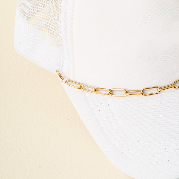 A close-up of The Darling Effect's Paperclip Chain-Gold Trucker Hat Chain attached to a white mesh trucker hat, displayed against a light beige background.
