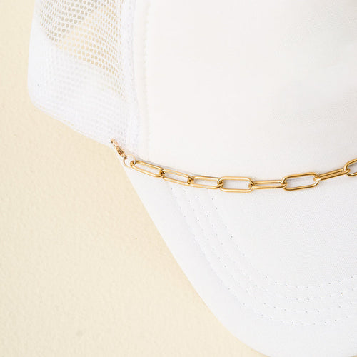 A close-up of The Darling Effect's Paperclip Chain-Gold Trucker Hat Chain attached to a white mesh trucker hat, displayed against a light beige background.