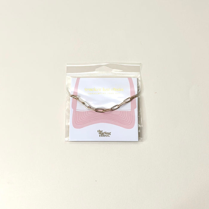 The Paperclip Chain-Gold Trucker Hat Chain by The Darling Effect is displayed on a branded card, making it the perfect accessory for your hat.