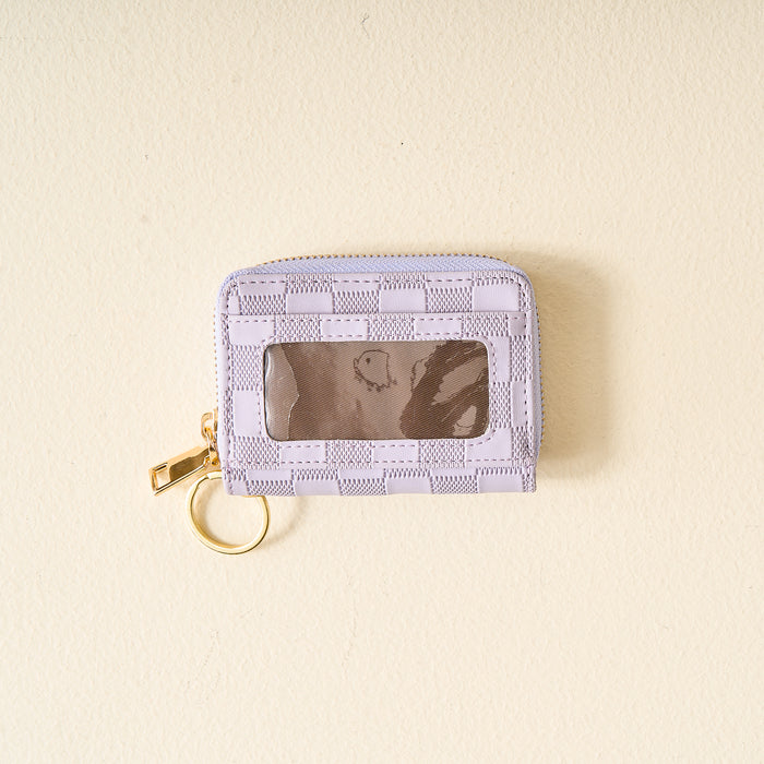The Darling Effect Periwinkle Check Zip Around Wallet, featuring a small periwinkle checkered design with multiple card slots, a clear ID window, gold zipper, and keyring, is placed on a light beige surface.
