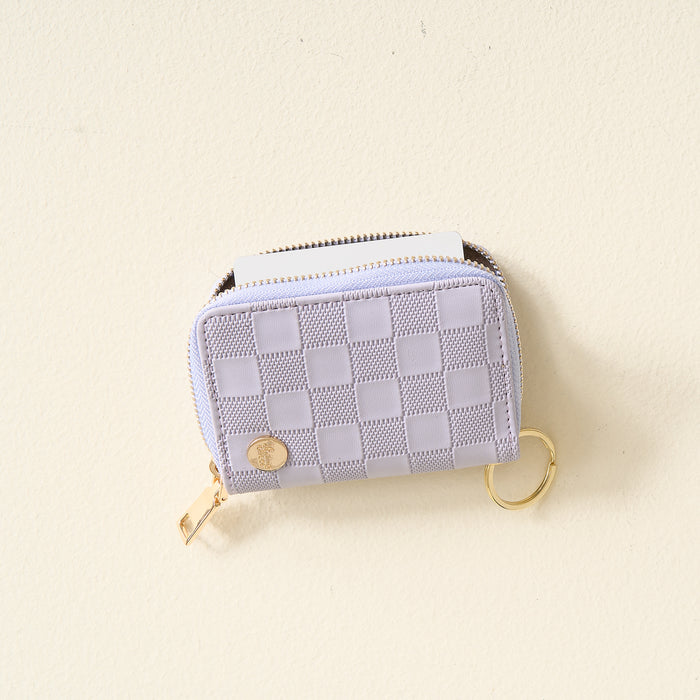 The Darling Effect Periwinkle Check Zip Around Wallet is a small, rectangular accessory with a checkered pattern, featuring convenient card slots, a gold zipper, and a gold keyring, displayed on a light, textured surface.