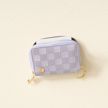 The Darling Effect Periwinkle Check Zip Around Wallet is a small, rectangular accessory with a checkered pattern, featuring convenient card slots, a gold zipper, and a gold keyring, displayed on a light, textured surface.