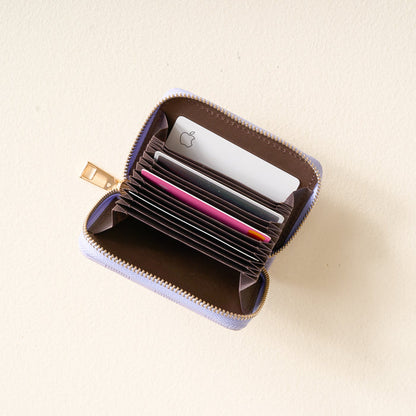 The Periwinkle Check Zip Around Wallet by The Darling Effect is shown open, revealing multiple card slots and a handy keyring, with various cards—including one featuring an Apple logo—organized inside and placed on a light-colored surface.