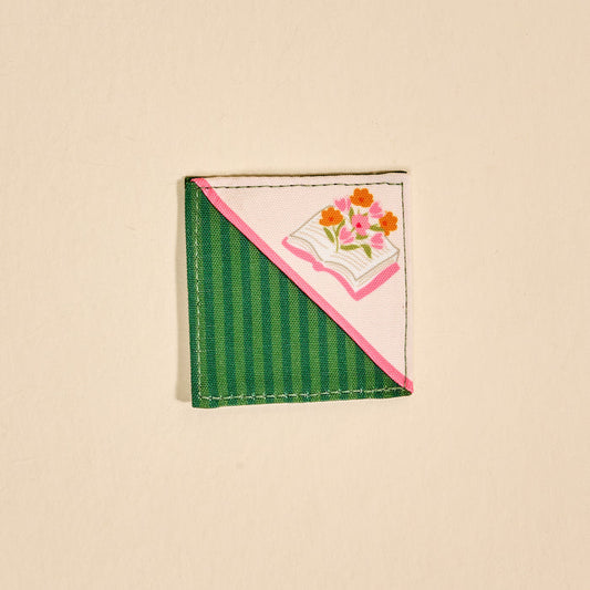 The Darling Effect's Petals & Pages Corner Keeper Fabric Bookmark features half green stripes, half pink, with an open book and floral design on light beige—making it a unique gift for book lovers.
